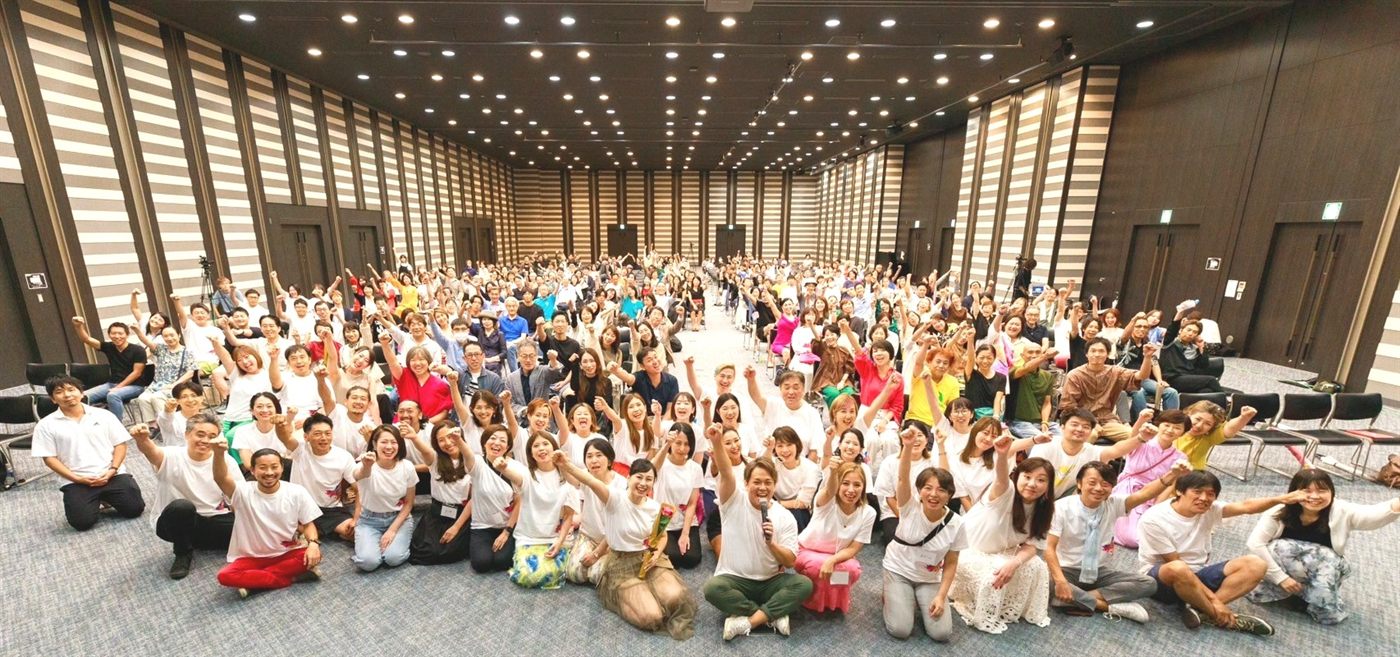 521名が参加したイベントの集合写真。会場いっぱいの参加者が手を挙げている様子。